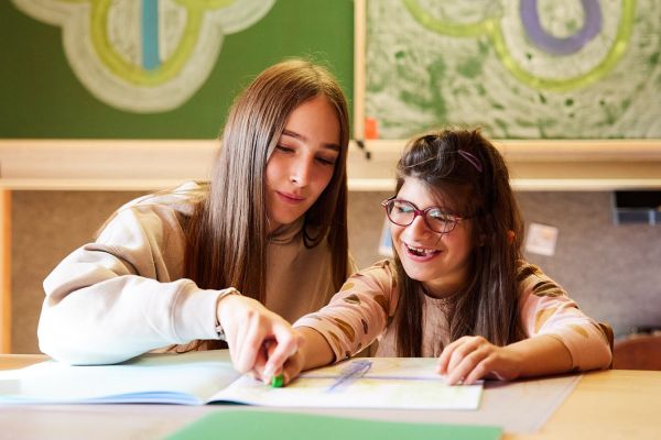 Eine Betreuerin hilft einer Schülerin beim Schreiben.